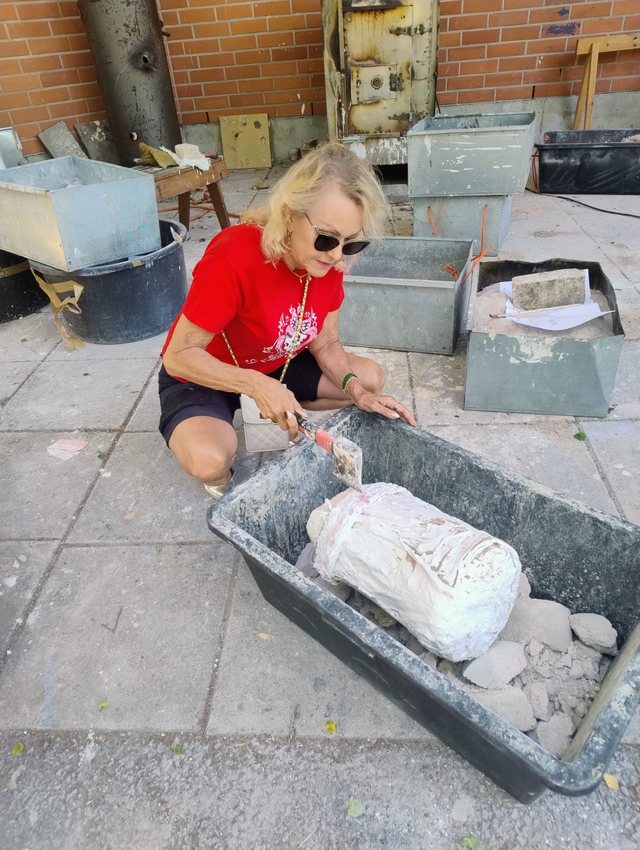 Aija Speville arbetar med en skulptur i en gjutlåda utomhus.